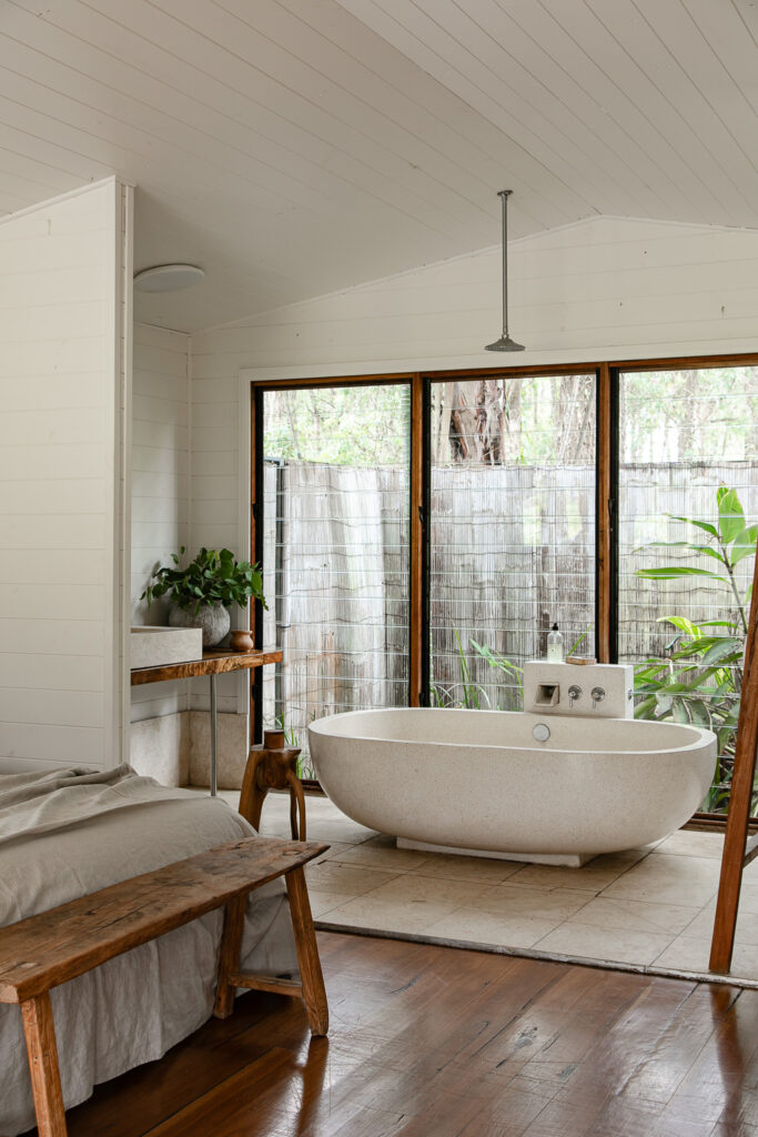 a stone bath and a king size bed in a well lit boathouse with rainforest backdrop